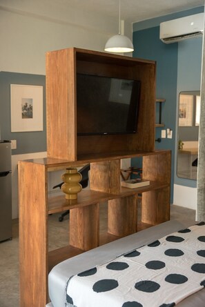 Een kamer met een houten entertainmentkast, een flatscreen televisie, een bed met een geborduurd sprei en een airconditioningsysteem dat aan het plafond is bevestigd.