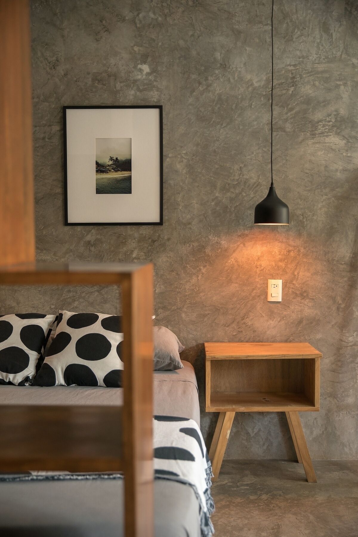 Une chambre à coucher avec un lit, une table de chevet, une lampe suspendue et un tableau encadré au mur.