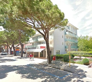 A street with a row of trees, a building with a sign that reads 'FREESB', and a sidewalk with a blue line marking. - Holiday apartment mit Klimaanlage und Balkon (Jesolo)