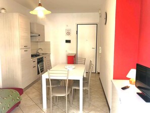 Een compacte keuken met een eettafel en stoelen, een kleine televisie, en een rode accentmuur.