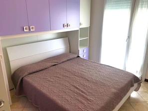 A bedroom with a bed, a wardrobe, and a window with curtains. - Holiday apartment mit Klimaanlage und Balkon (Jesolo)