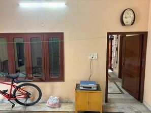 Une pièce avec un vélo, une petite armoire contenant un lecteur DVD et une porte donnant sur une autre pièce.
