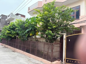 A residential building with a gated entrance, a metal fence, and a tree in front.