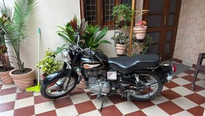 Een motorfiets op een zwart-wit geruite vloer, met potplanten en een deur op de achtergrond.