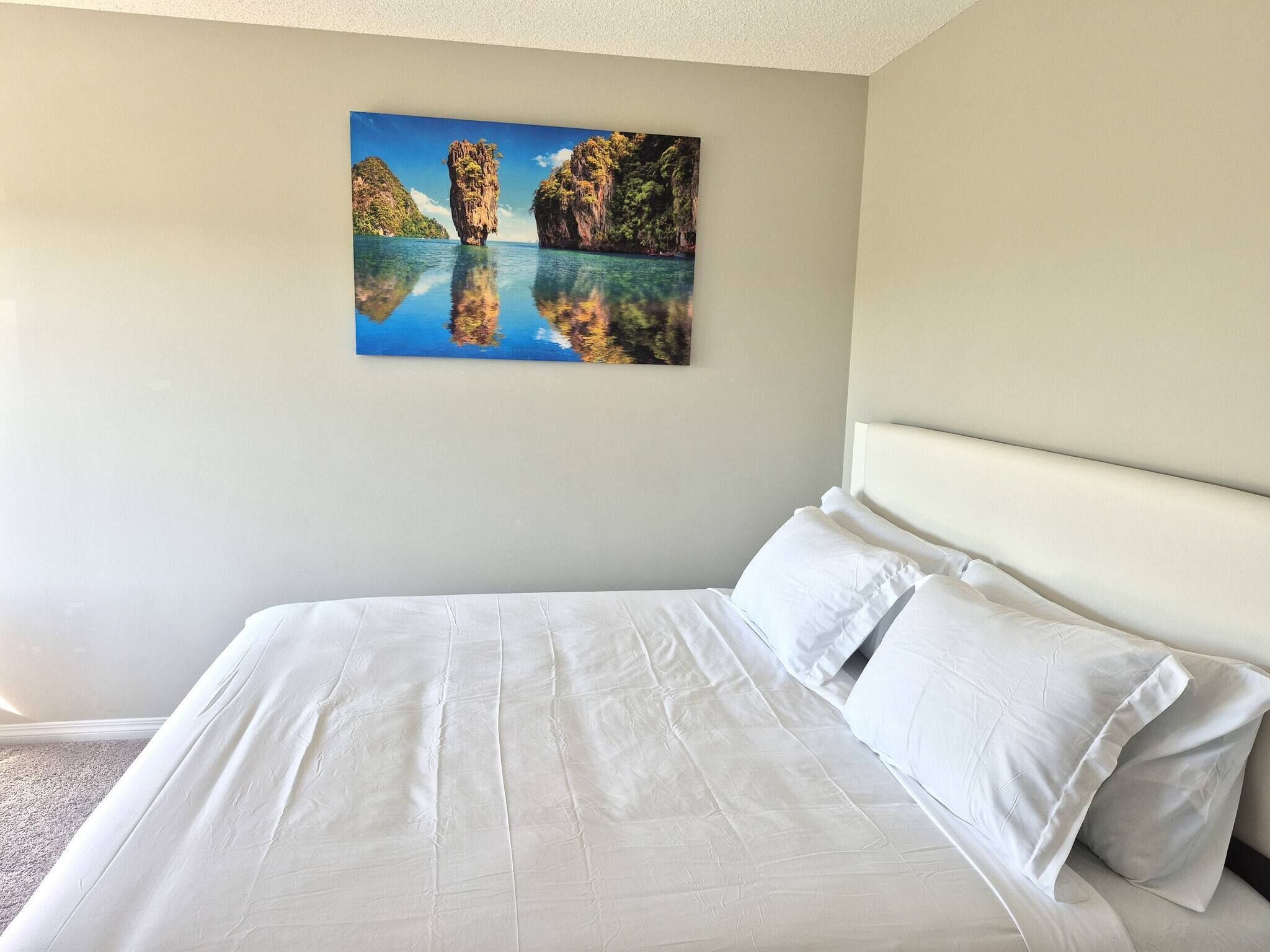 A hotel room with a large bed, white bedding, and a painting of a coastal landscape on the wall.