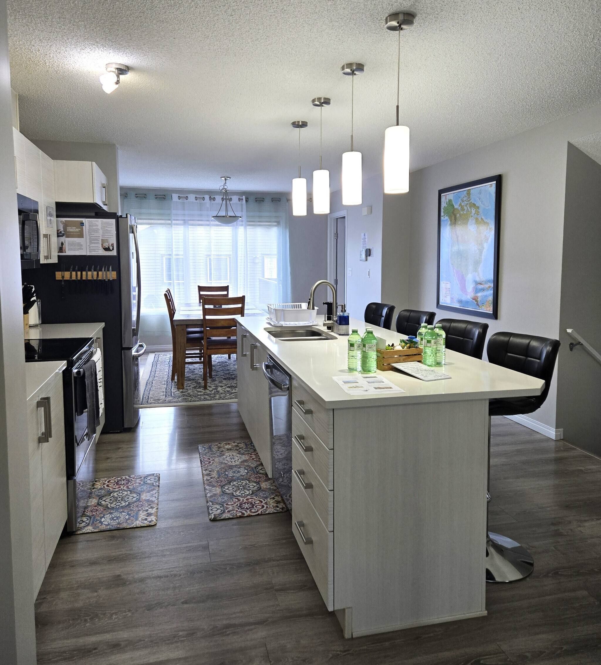 A modern kitchen with a central island, a dining area with chairs, and a large window providing natural light.