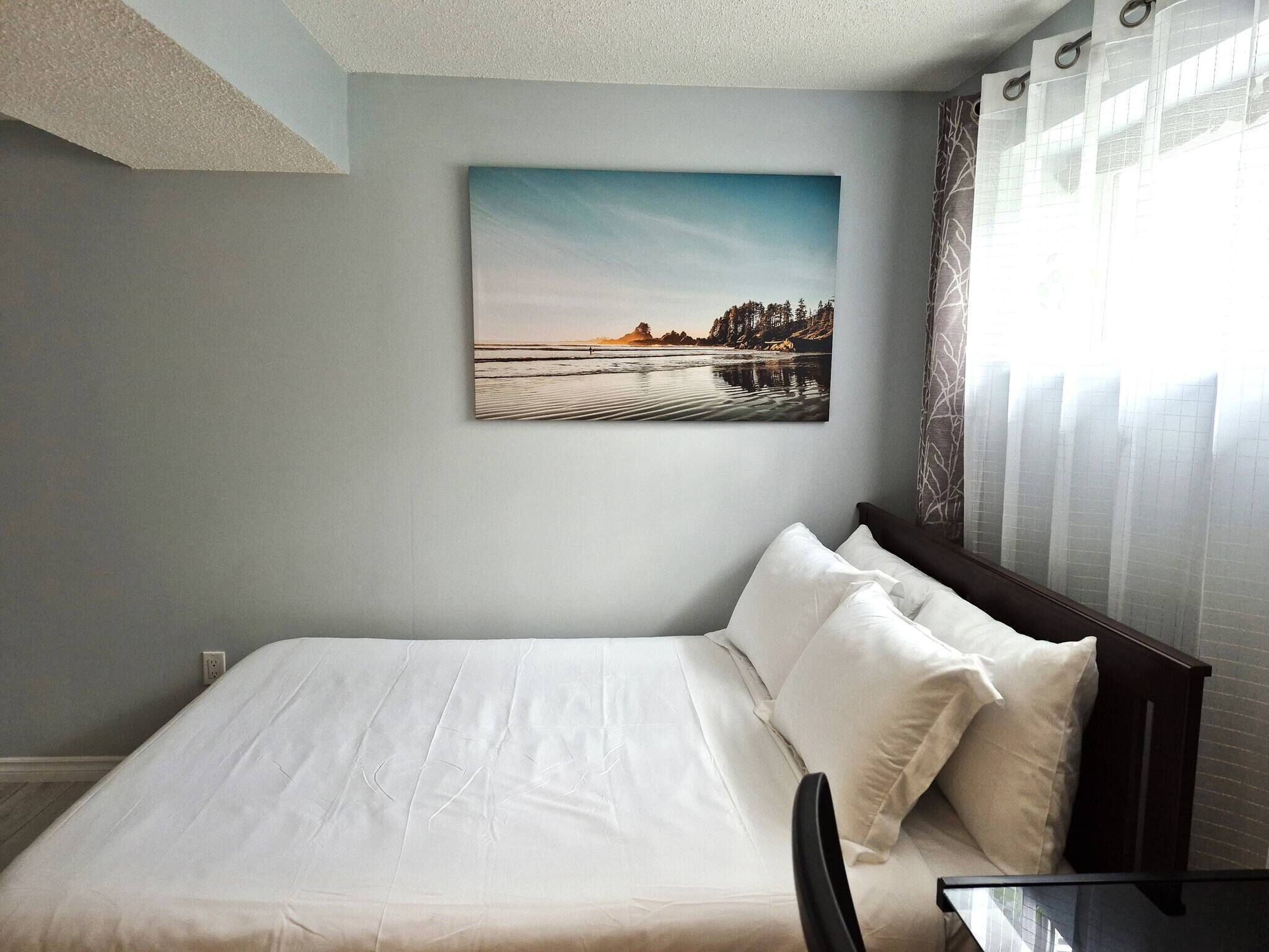 A bedroom with a bed, pillows, a bedside table, and a painting of a landscape.