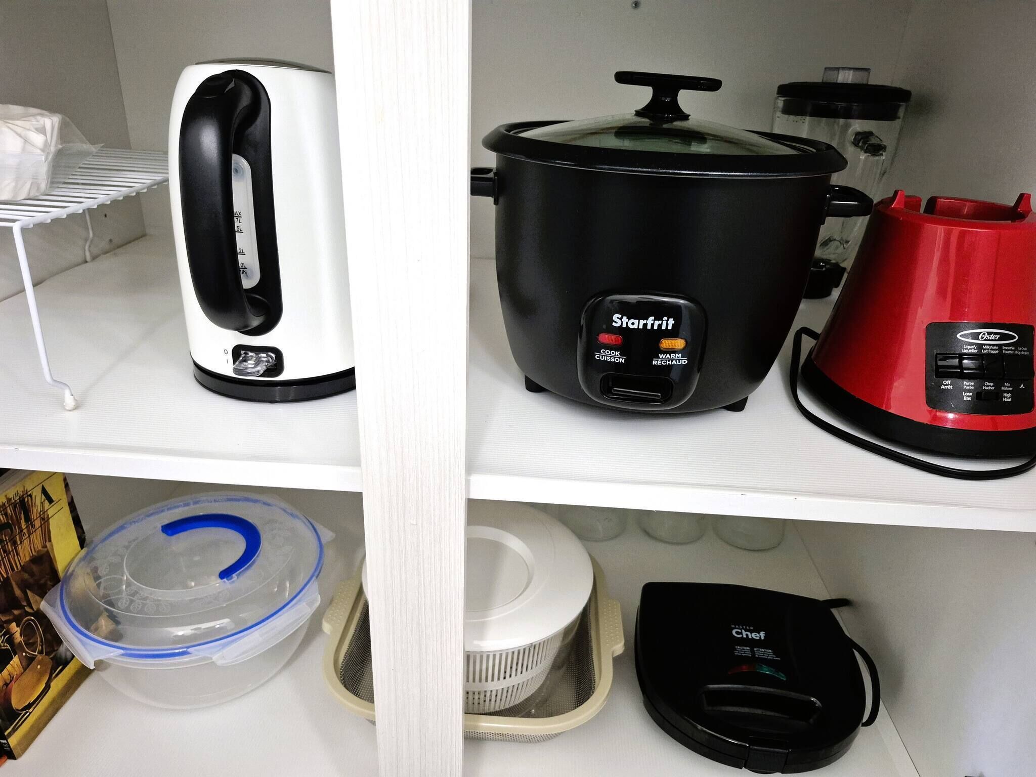 A kitchen shelf with a coffee maker, a slow cooker, a red kettle, and a food processor.