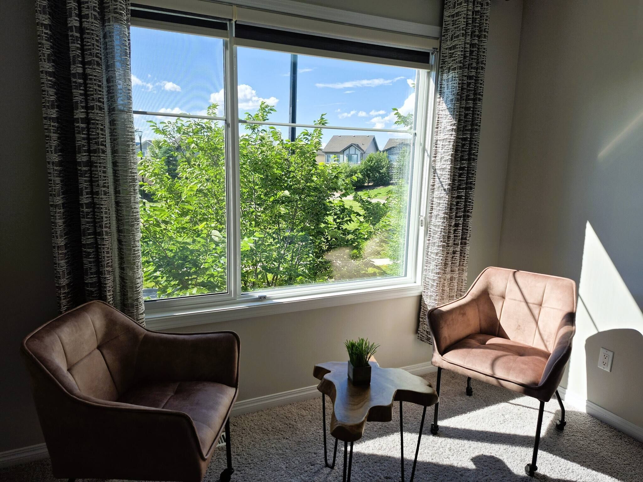 A room with two leather armchairs, a small table with a plant, and a large window with curtains.
