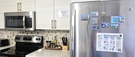 Eine moderne Küche mit Edelstahlgeräten, darunter Mikrowelle, Backofen und Kühlschrank. Es sind Holzschränke und eine Arbeitsplatte mit verschiedenen Küchenutensilien zu sehen.