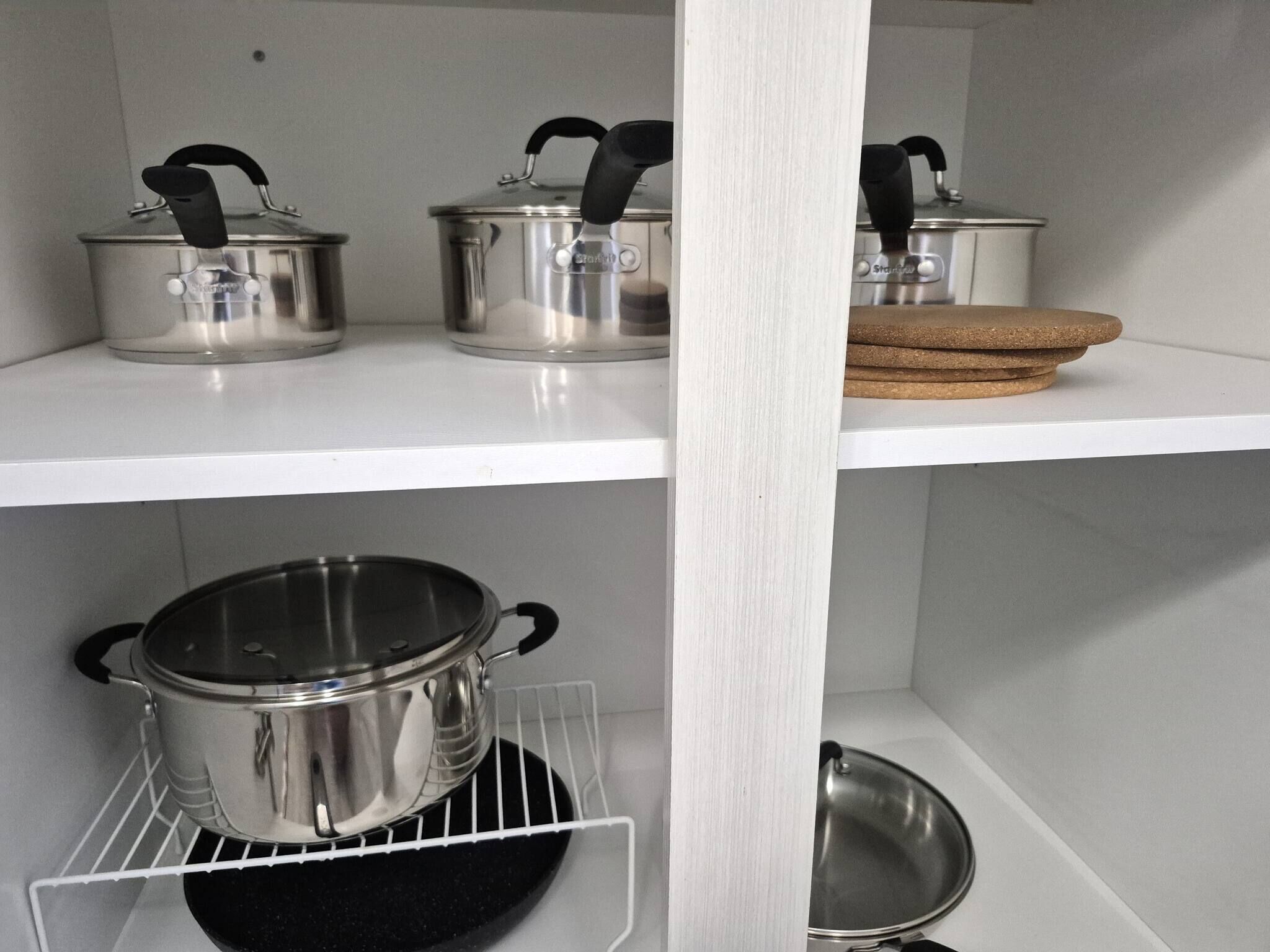 Ett kök med kastruller i rostfritt stål på hyllor och ett kastrullställ.