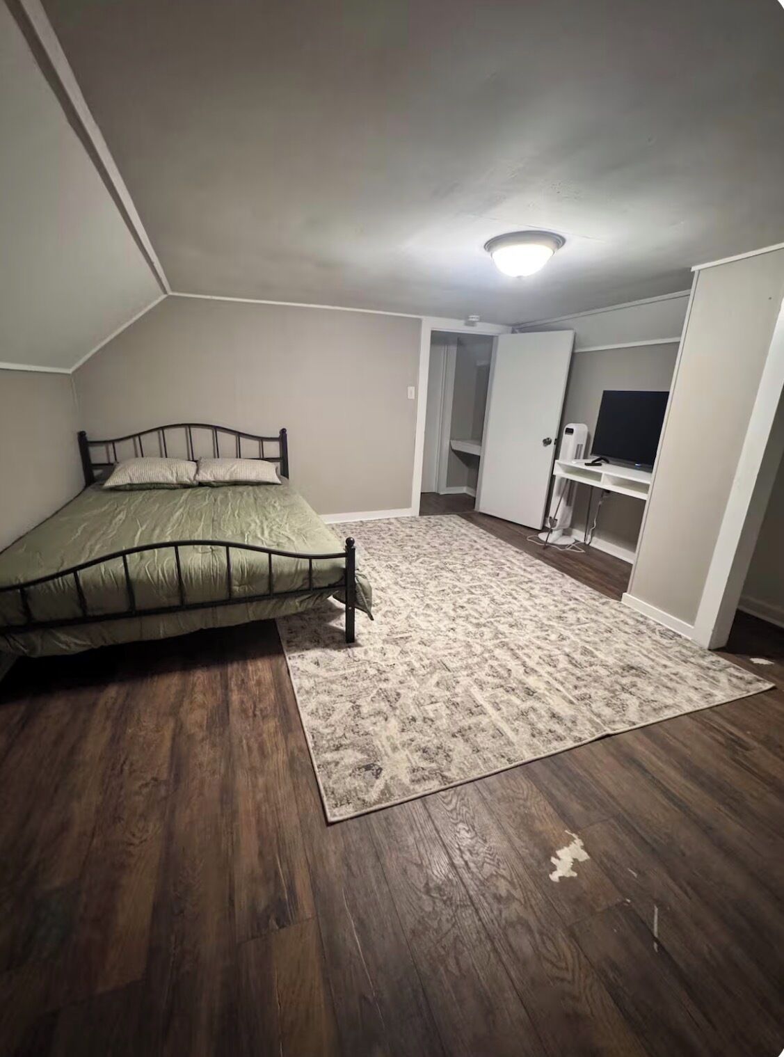 Quarto com cama, uma pequena escrivaninha e televisão.