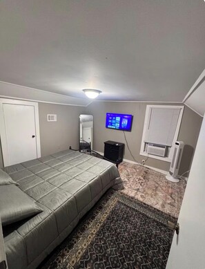 A bedroom with a bed, a television mounted on the wall, a heater, and a window with blinds.
