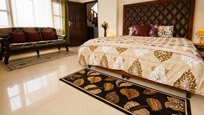 Habitación de hotel con una cama grande, un sofá, una alfombra y una puerta que da a otra habitación.