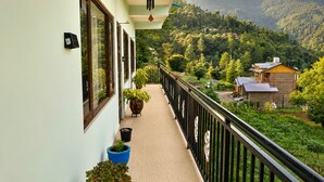 Un balcón con vista a un paisaje montañoso, plantas en macetas y una estructura de madera al fondo.