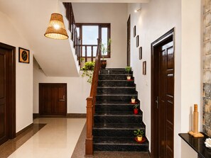 A staircase with wooden railings and potted plants, leading to a landing with a large window. - Adorable 3-bedroom luxury house with modular kitchen in peaceful Jutogh (Jutogh)