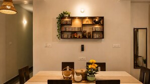Un comedor con una mesa dispuesta para cuatro personas, una estantería arriba y una lámpara colgante.