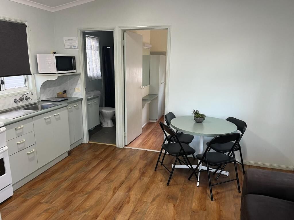 Une cuisine compacte équipée d’un four à micro-ondes, d’un évier et d’une cuisinière, un coin repas avec une table et des chaises, et une salle de bain séparée, visible à travers une porte ouverte.