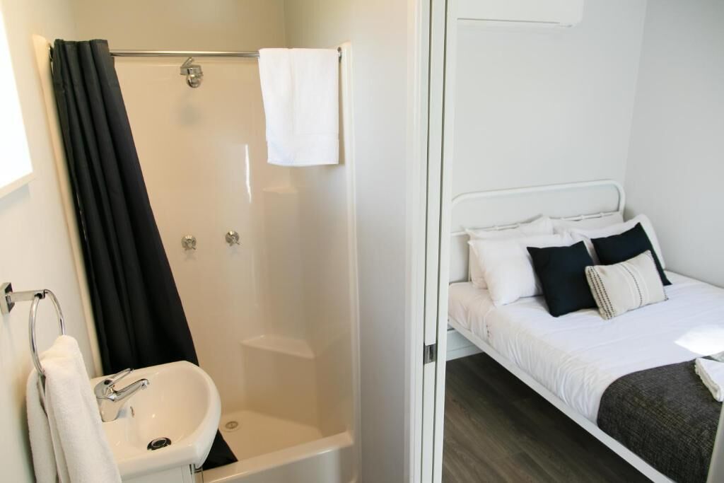 Habitación de hotel con ducha, lavamanos y cama con almohadas.