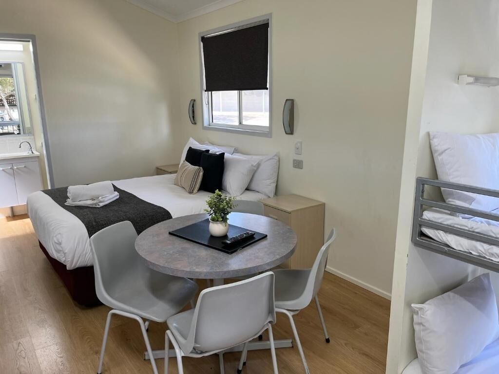 Een compacte hotelkamer met een bed, nachtkastje en een kleine ronde tafel met stoelen.