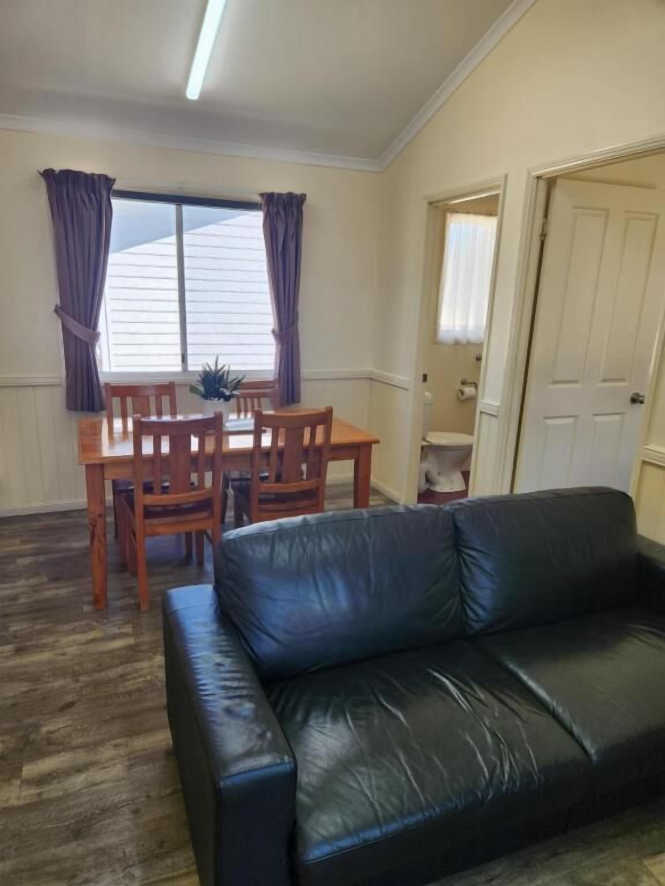 A room with a dining table and chairs, a black leather sofa, and a door leading to another room.