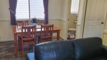 A room with a dining table and chairs, a black leather sofa, and a door leading to another room.