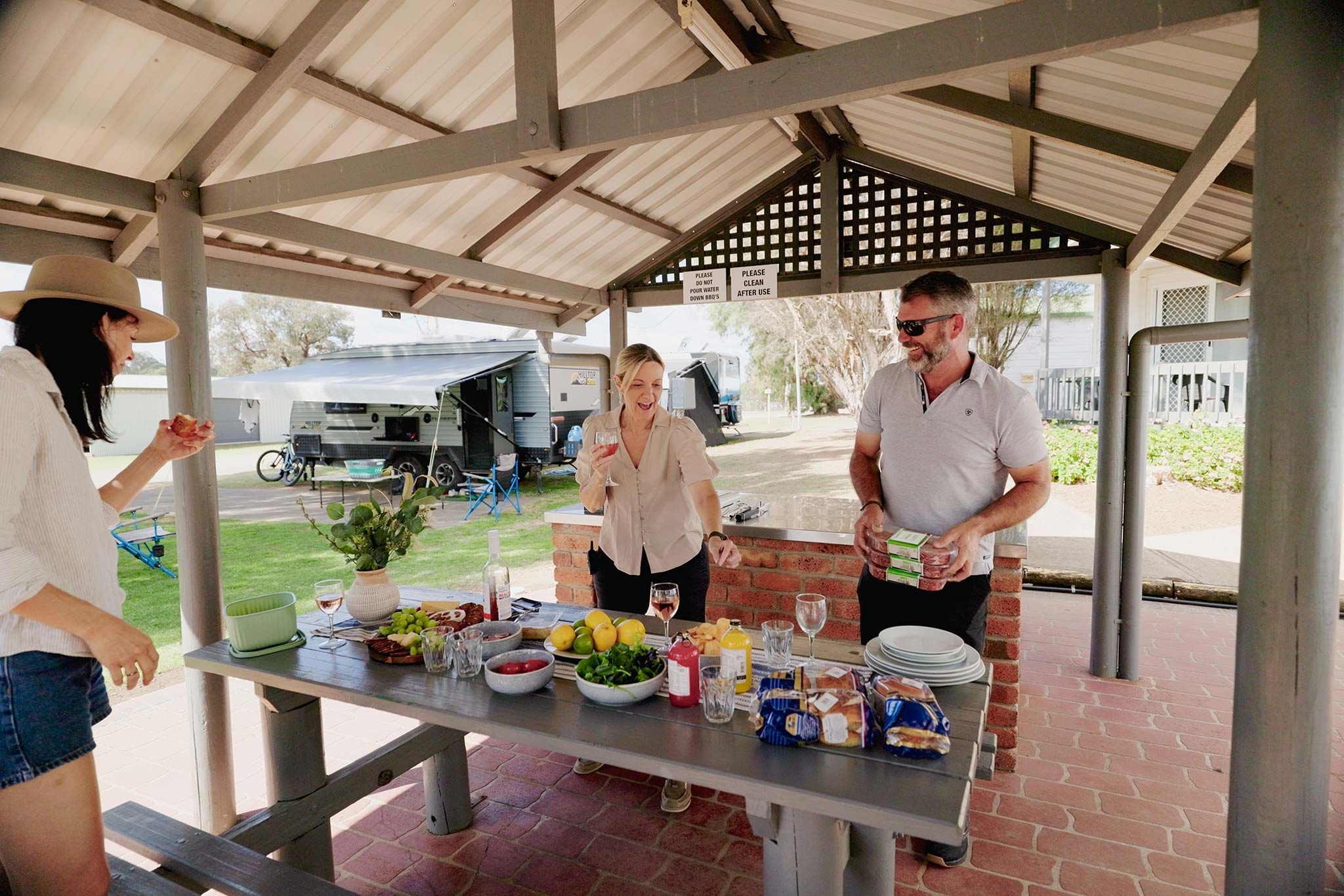 A covered outdoor area with a table set for a meal, a grill, and a tented RV in the background.