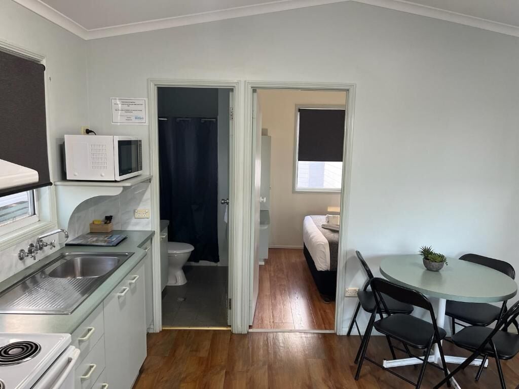 A compact kitchen with a microwave, sink, and stove, leading to a bathroom with a shower curtain.