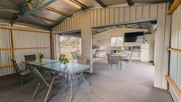 A spacious indoor area with a large table and chairs, a kitchen area with appliances, and a view through a door.