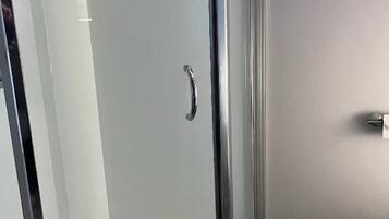 A glass-enclosed shower area with a door handle, adjacent to a toilet, in a bathroom with stone flooring.