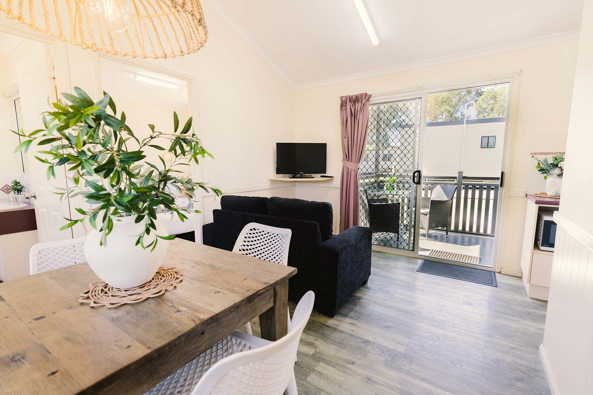 A living room with a wooden table, a TV, and a balcony with a view.