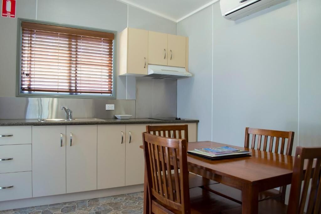 A compact kitchen with a dining table and chairs, a window with blinds, and a built-in stove.