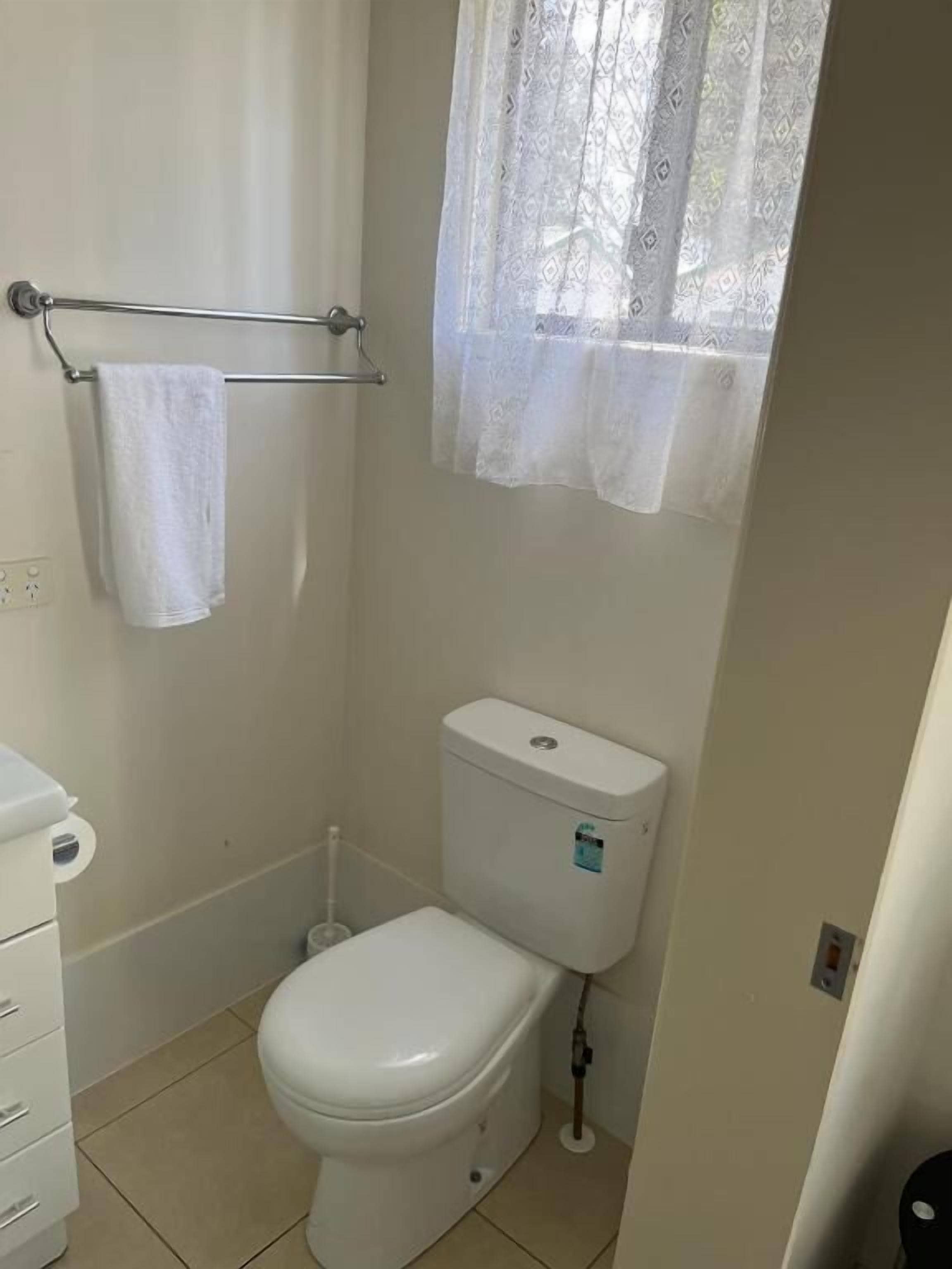 A small, clean bathroom with a toilet, a towel rack, and a window with a curtain.