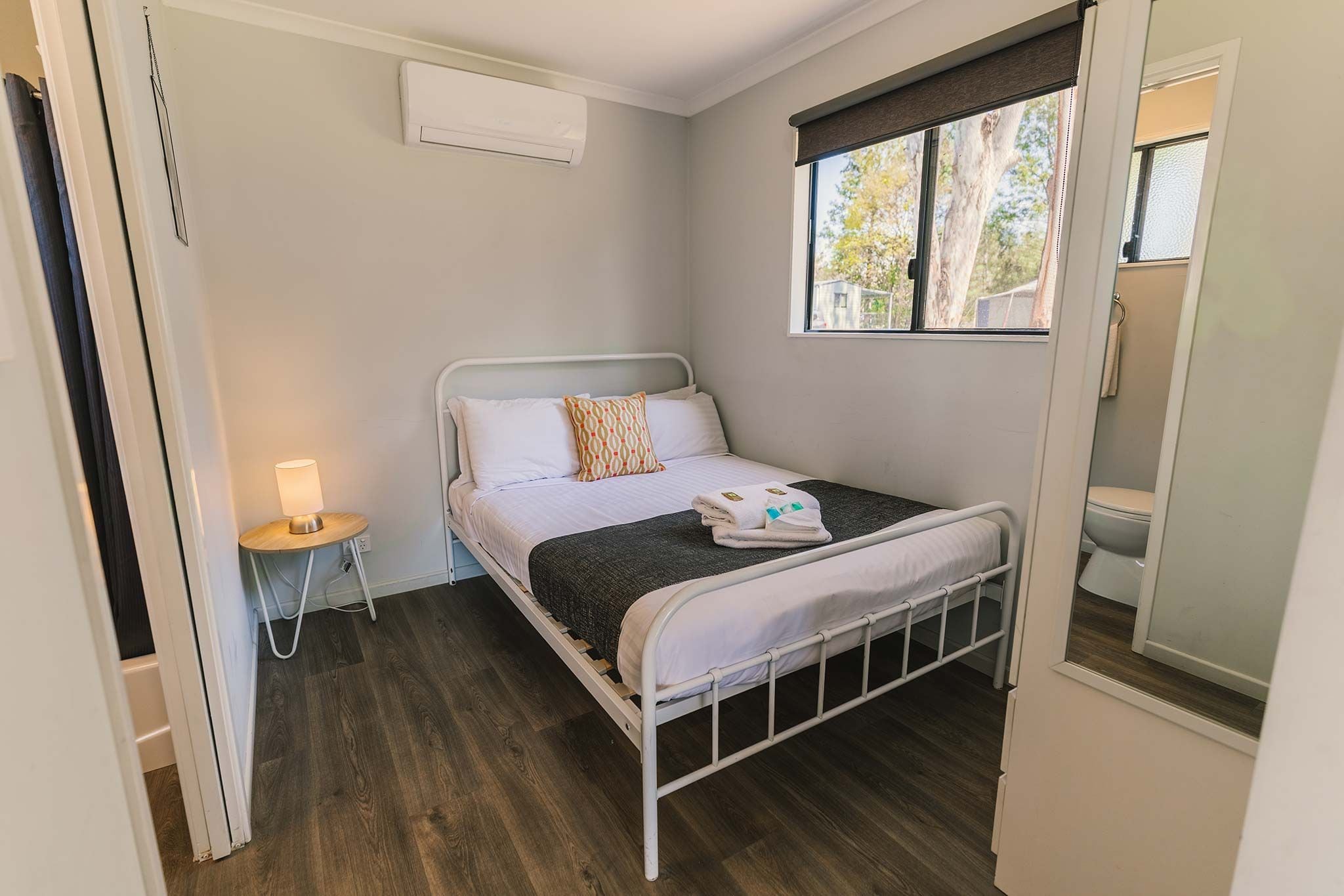 A single bed with a headboard, a bedside table with a lamp, and a window with a view of trees.