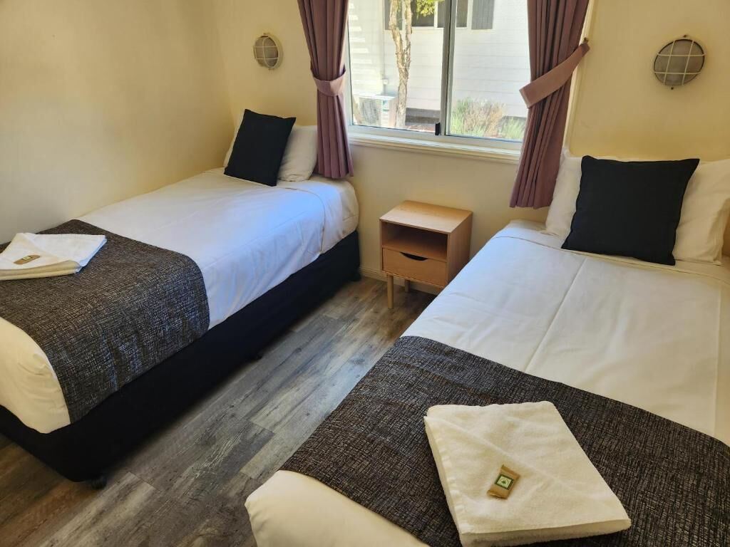 A room with two beds, a small wooden nightstand, and a window with curtains.