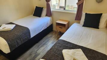 A room with two beds, a small wooden nightstand, and a window with curtains.