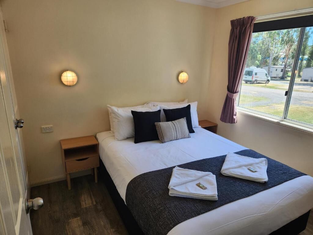 A hotel room with a bed, bedside tables, and a window with curtains.