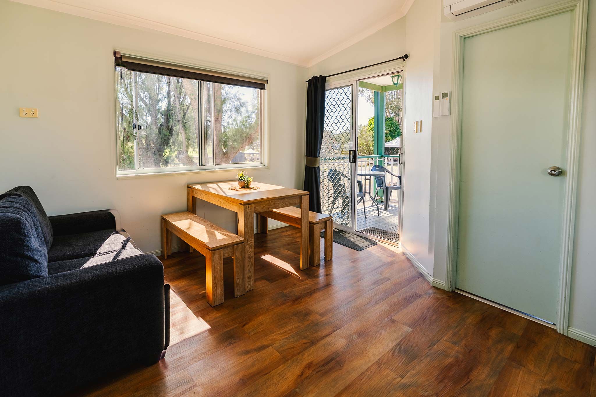 A room with a wooden table and chairs, a sofa, and a door leading to a balcony.