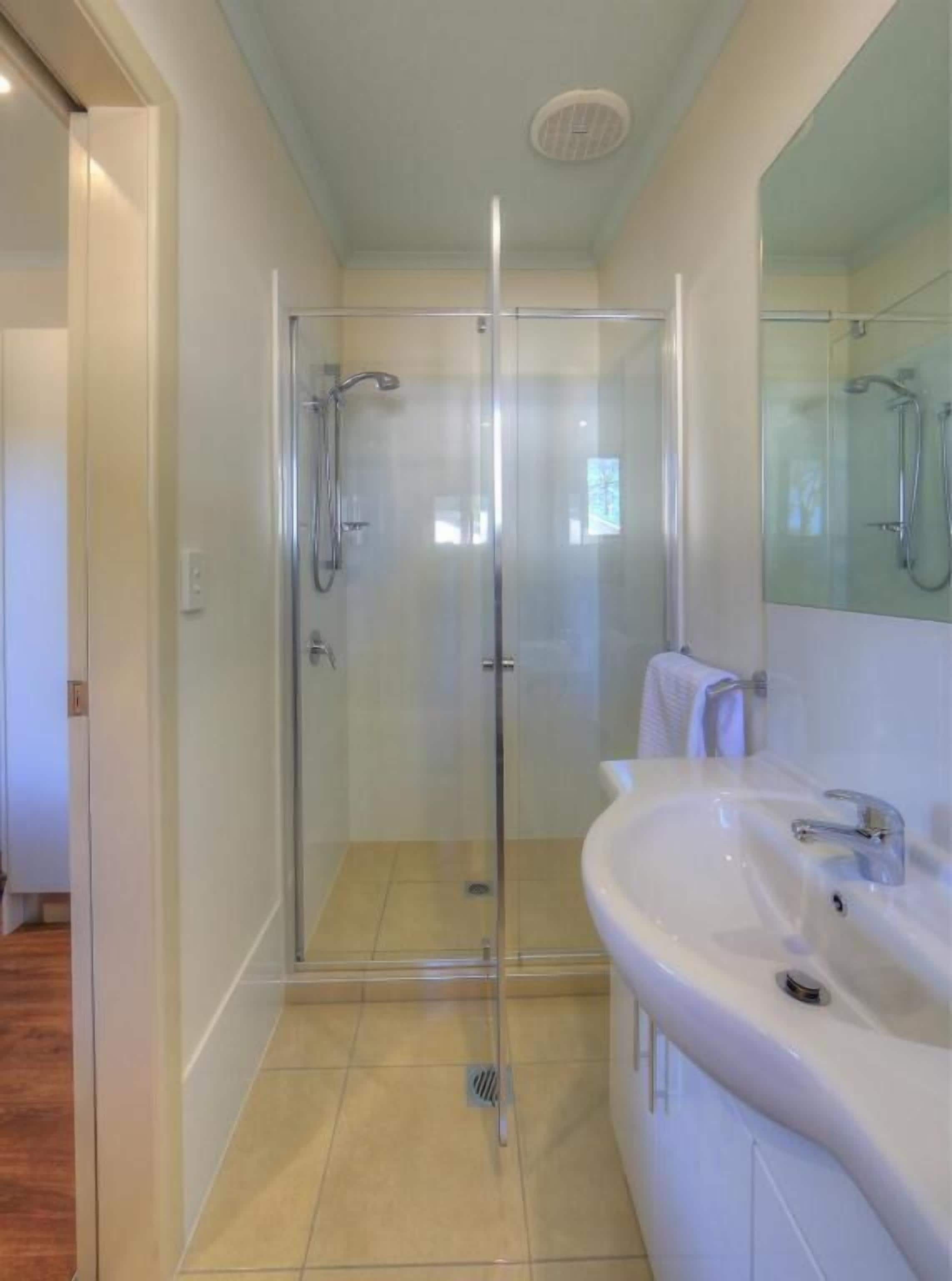 A modern bathroom with a glass-enclosed shower, a white sink, and a mirror.