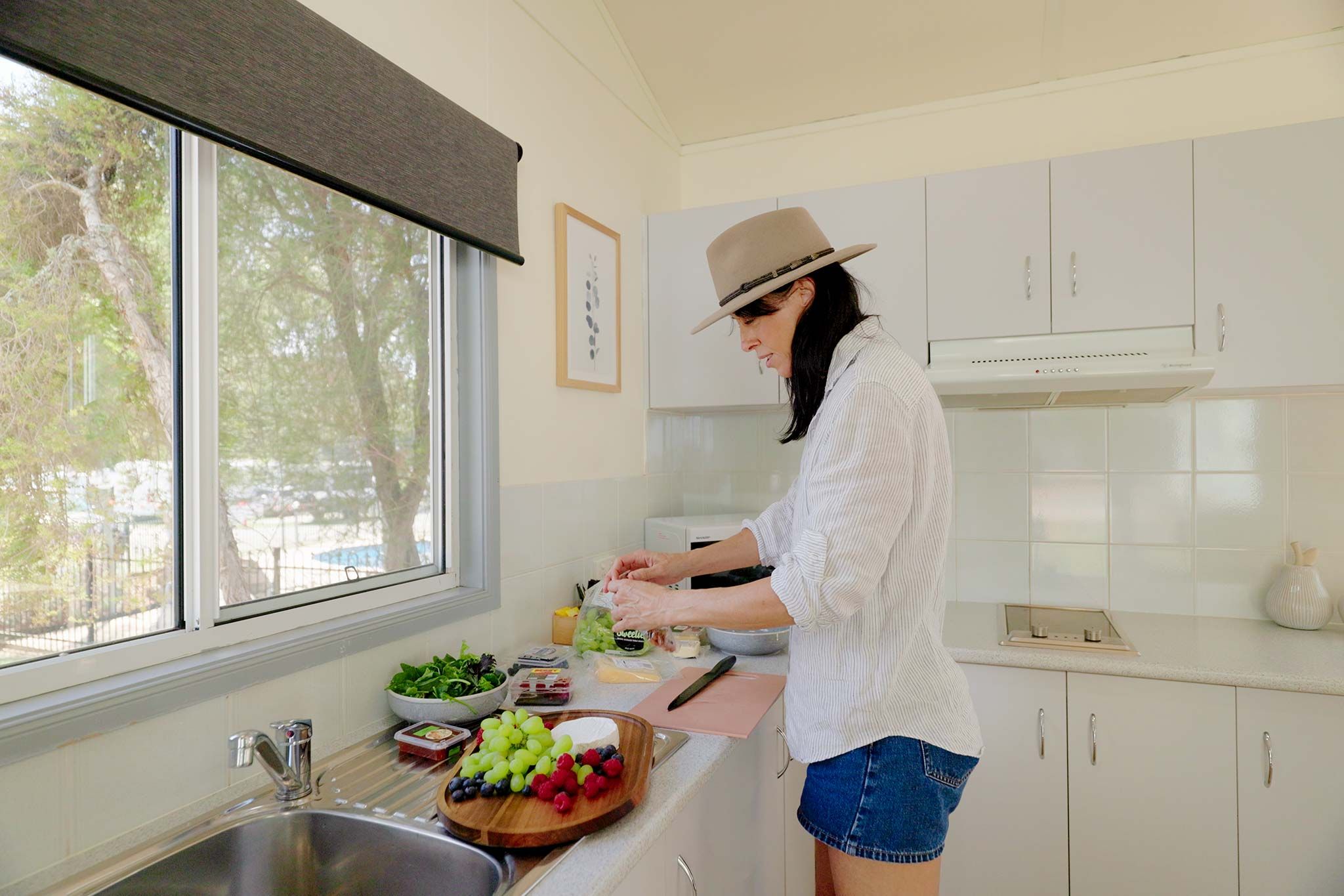 A person in a kitchen preparing food with a window, white cabinets, and a sink.