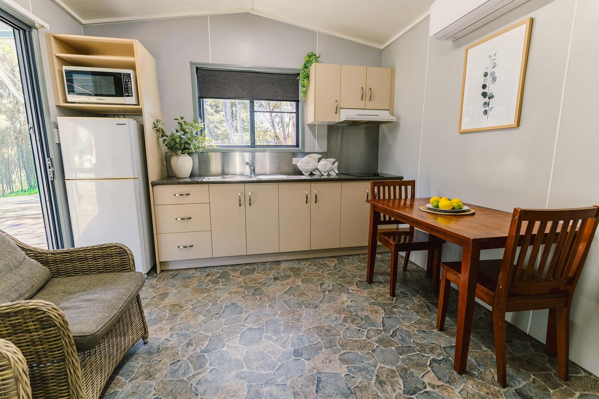 A compact kitchen with a stone floor, a dining table with chairs, a microwave, and a refrigerator.