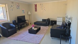 En stue med et fladskærms-tv, to sofaer, et sofabord med blomster og dekorativ vægkunst.