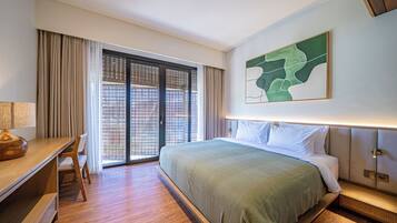 Habitación de hotel con cama, escritorio, silla, ventana grande con cortinas y una obra de arte colgada en la pared.