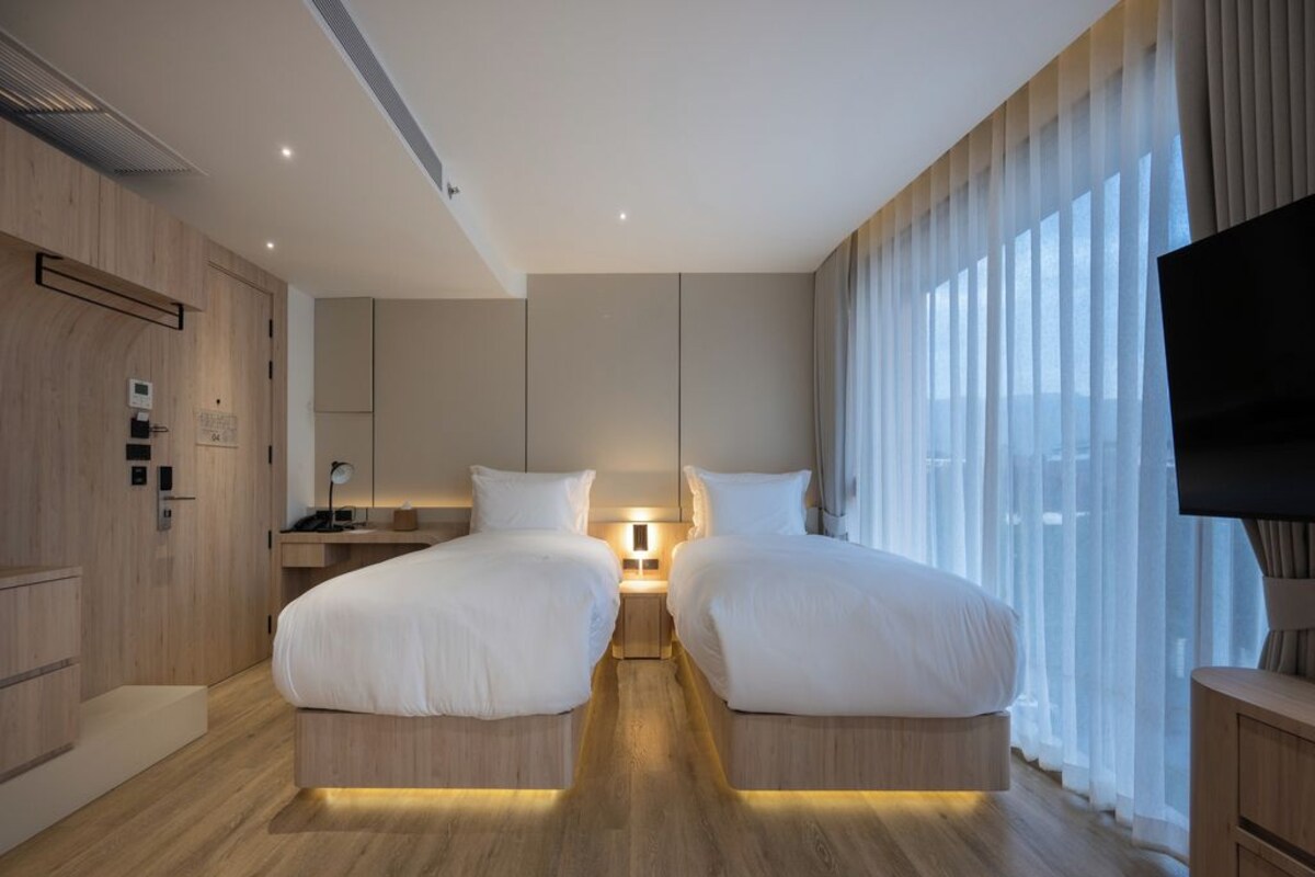 A hotel room with a double bed, bedside tables, a TV, and a large window with curtains.