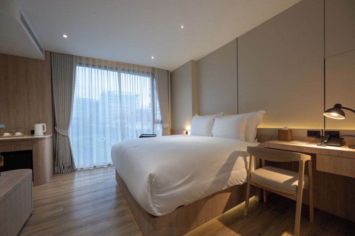 A hotel room with a large bed, a desk, a chair, and a window with curtains.