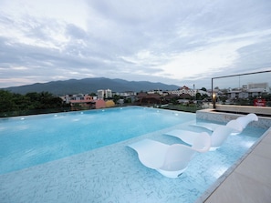 A swimming pool with clear blue water, surrounded by a tiled deck with white lounge chairs. - HOLM HOTEL CHIANGMAI (Chiang Mai)