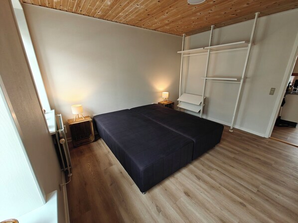 A bedroom with a bed, bedside lamps, a wooden floor, and a white wardrobe.