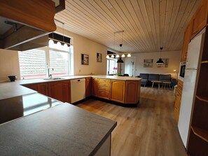 A modern kitchen with wooden cabinets, a dishwasher, and a dining area with a sofa and table.