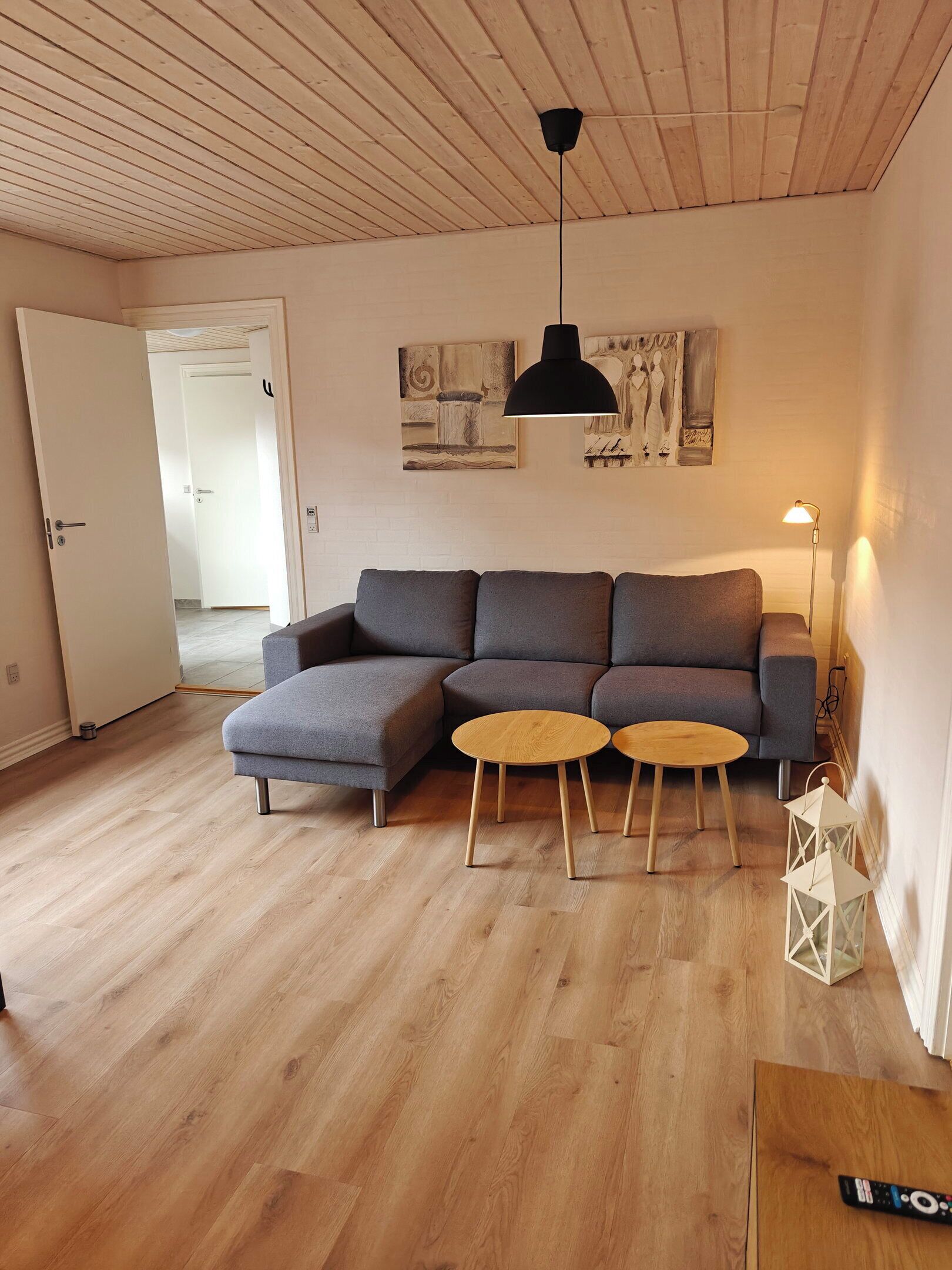 A living room with a sectional sofa, two small wooden tables, a black pendant light, and a white lantern.
