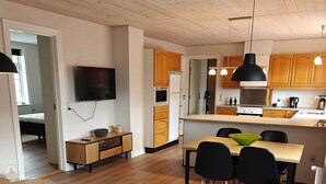 A modern kitchen with wooden cabinets, a dining area with a table and chairs, and a living room with a sofa and a TV.